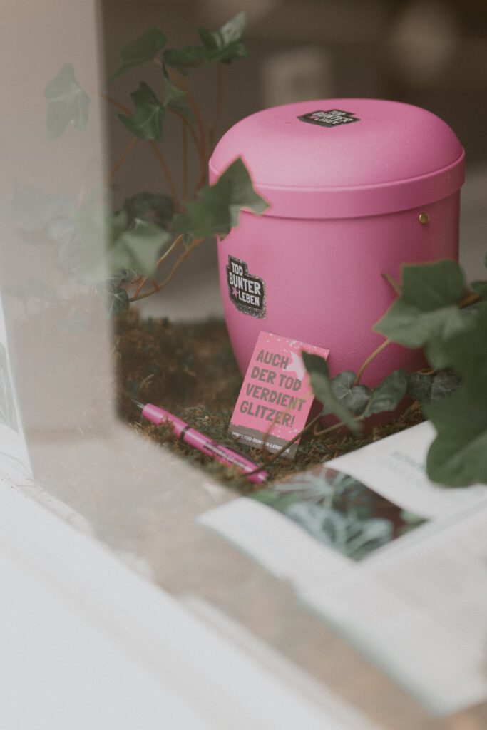 Rosa Urne mit Aufkleber und einer Karte mit der Aufschrift Auch der Tod verdient Glitzer im Schaufenster